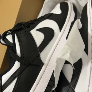 Nike Dunk Low i svart och vit - Säljer ett par Nike Dunk Low i klassisk svart och vit färgkombination. Skorna är i nytt skick och kommer i originalkartong. Perfekta för både vardag och fest med sin stilrena design och bekväma passform. Köpta 13/11-23 säljer pågrund av fel storlek. Möts i Stockholm 