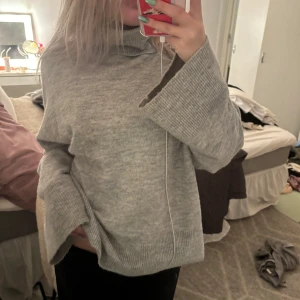 Grå stickad tröja - Mysig grå stickad tröja med polokrage. Perfekt för kyliga dagar med sin lösa passform och långa ärmar. Ribbstickade detaljer vid ärmslut och nederkant ger en extra touch. Superbekväm och stilren!