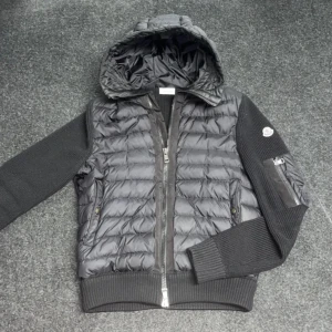 Svart pufferjacka med huva - Säljer en snygg svart pufferjacka med huva. Jackan har en quiltad design och dragkedja framtill. Ärmarna är ribbade och har en cool ficka med dragkedja på ena sidan. Perfekt för höst och vinter!