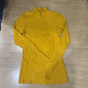 Gul ribbad polotröja - Säljer en snygg gul polotröja i ribbat material. Perfekt för höst och vinter med sin varma och mysiga känsla. Tröjan har långa ärmar och en tight passform som sitter fint på kroppen. Ett måste i garderoben för att liva upp de mörka dagarna! 💛