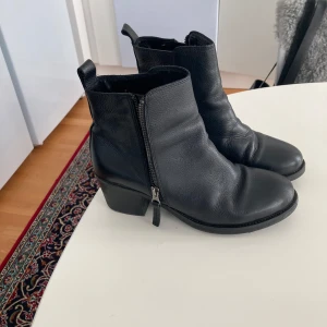 Roots Svarta boots med dragkedja I stl 39 - Snygga svarta boots från Roots i skinn med dragkedja på sidan. Perfekta för höst och vinter med en robust sula för bra grepp. De har en klassisk design som passar till det mesta. Använda men i bra skick, redo för nya äventyr!