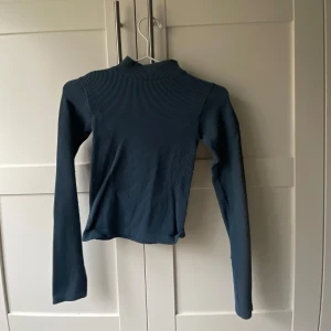 Mörkblå ribbad tröja med öppen rygg - Säljer en snygg mörkblå ribbad tröja med en cool öppen rygg. Perfekt för både vardag och fest! Tröjan har långa ärmar och en tight passform som framhäver figuren. Den är i  bra skick och redo för nya äventyr. Passar perfekt till jeans eller kjol!