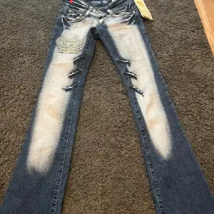 Intresskoll för mina Snygga jeans från Crazy Age i blått med coola slitningar och en broderad krona på ena benet. De har en extrem låg midja och en bootcut passform. Midjemått:32/34 ytterbenslängden: 100 innebenslängden:94❤️