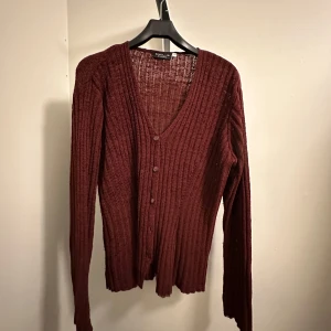 Vinröd ribbad kofta - En snygg vinröd kofta i ribbat och varmt material från Kappahl i storlek 42/44. Den har en v-ringad design med knappar framtill och långa ärmar. Oanvänd!