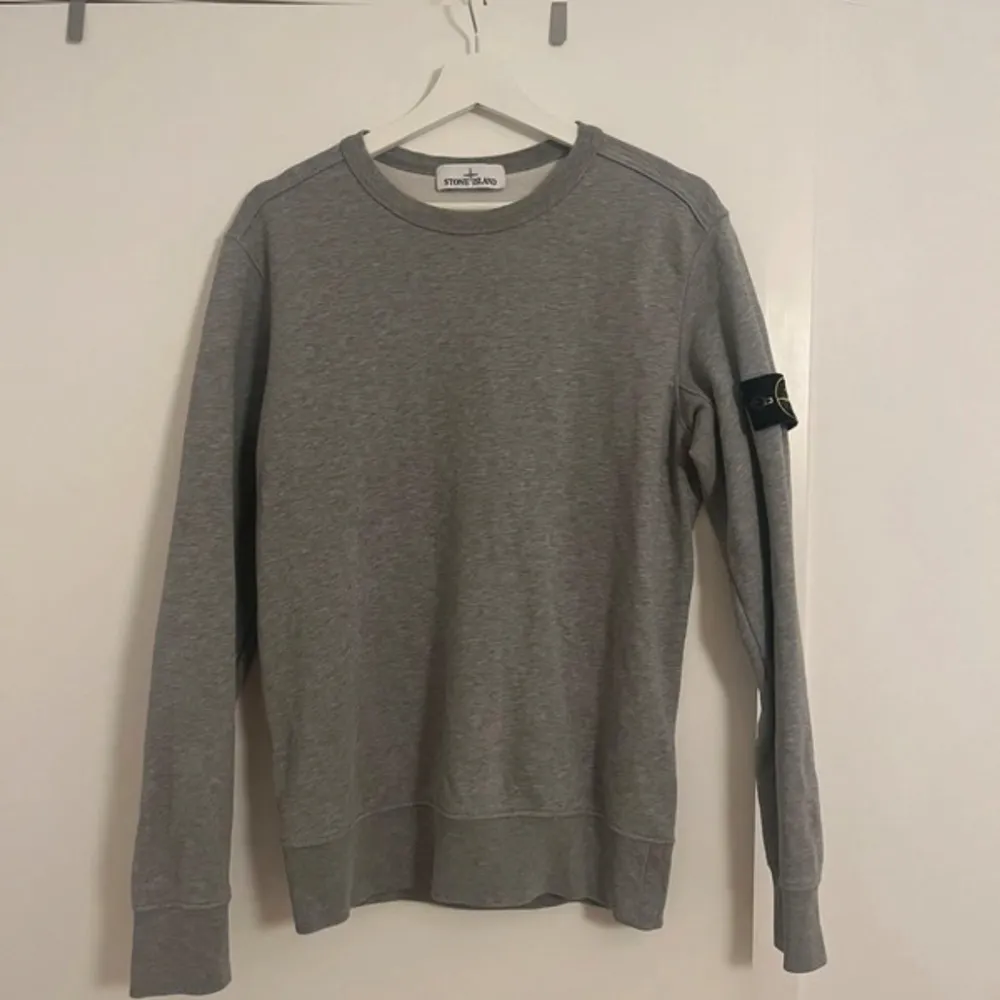 Säljer en snygg grå sweatshirt från Stone Island i mycket bra skick. Den har en klassisk rund hals och långa ärmar med det ikoniska Stone Island-märket på ärmen. Perfekt för både vardag och chill dagar. Passar till allt och är superbekväm!. Tröjor & Koftor.