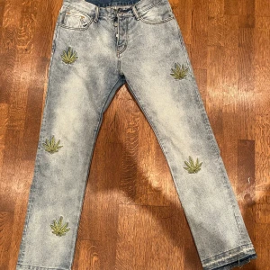 Jeans med broderade detaljer från mnml - Säljer ett par snygga jeans från mnml i ljusblå tvätt. De har coola broderade lövdetaljer på både fram- och baksidan. Perfekta för en avslappnad stil med en twist. De är i bra skick och passar perfekt för både vardag och fest. Hör av er vid intresse eller frågor