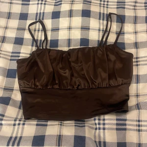 Brun satinlinne, topp - Säljer ett snyggt brunt satinlinne med smala axelband från HM. Plagget är i väldigt bra skick så det inte har kommit till användning så ofta och är inte längre min stil. 