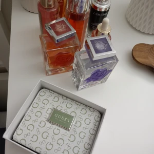 Vit plånbok från Guess - Säljer en snygg vit plånbok från Guess med deras ikoniska logotypmönster. Plånboken har en dragkedja och flera fack för kort och kontanter. Perfekt för att hålla ordning på dina saker med stil! Kommer i originalförpackning.