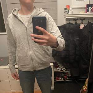 Säljer en grå hoodie i bra skick. Den har en dragkedja framtill och är perfekt för vardagsbruk. Passar bra till jeans eller träningsbyxor. Skön och enkel stil för alla tillfällen. Från lager 157