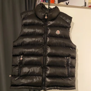 Svart dunväst från Moncler - Säljer en snygg svart dunväst från Moncler i mycket bra skick. Västen har en quiltad design med dragkedja och två fickor fram. Perfekt för höst och vinter, håller dig varm och stilren. Vid frågor och funderingar är de bara att skriva.