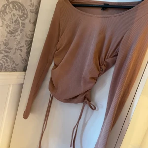 Beige ribbad topp med knytning - Säljer en superfin beige ribbad topp med långa ärmar. Toppen har en snygg knytning i midjan som ger en fin passform. Perfekt för både vardag och fest! 💛
