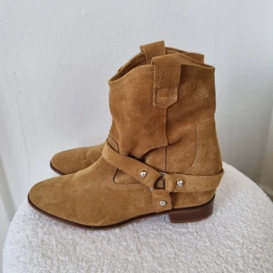 Bruna Mockaboots - Säljer ett par snygga bruna boots i mocka från H&M. De är i lite cowgirl-stuk och har några enstaka fläckar. De är tyvärr lite för stora för mig men tror de hade varit så snygga till både sommaren och hösten till typ en vit midi-kjol så man lutar lite åt countrystilen!! 🐎