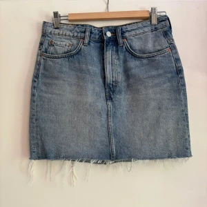 Jeanskjol från Weekday - Säljer en snygg jeanskjol från Weekday i storlek 38. Kjolen är i en klassisk blå jeansfärg och har en rå kant längst ner. Den är välanvänd men i fint skick!