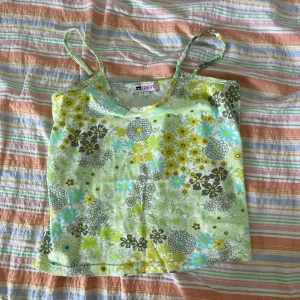 Blommig linnetopp från Gianini - Säljer en superfin blommig linnetopp från Gianini i storlek L. Toppen har ett färgglatt mönster med blommor i grönt, gult, blått och vitt. Den är ärmlös med smala axelband och är perfekt för sommarens sista dagar! 