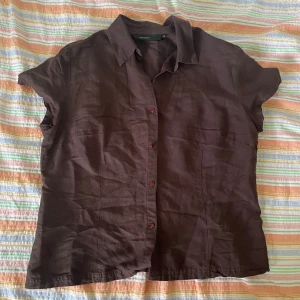 Brun kortärmad skjorta från KappAhl - Säljer en brun kortärmad skjorta från KappAhl i storlek 46. Skjortan har en klassisk krage och knappar framtill. Den är i bra skick och redo för en ny ägare!