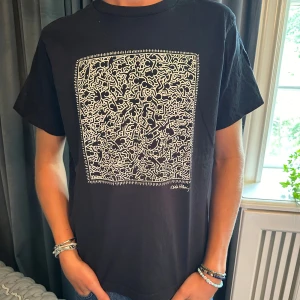 Svart t-shirt med konstnärligt tryck - Säljer en svart t-shirt med ett coolt konstnärligt tryck på framsidan. T-shirten är kortärmad och har en normal passform. Perfekt för vardagsbruk eller att styla upp för en fest. Passar både killar och tjejer!
