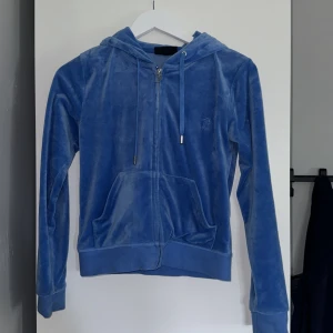 Blå hoodie från Juicy Couture - Säljer en snygg blå hoodie från Juicy Couture i storlek S men passar XS och M också! har använt 1-2 gånger tror jag och är i väldigt fint skick förutom om liten liten fläck som man ser på en av bilder men har inte tänkt på den innan! 