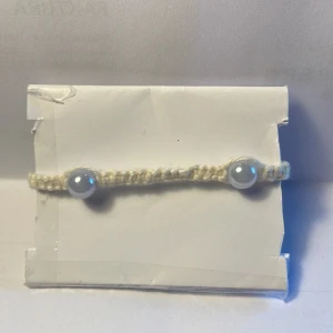 Armband -  Han gjorde armband i bomull och pärlor som detaljer, man kan ändra storleken, armarna det är 0,5 cm brett. Armbandet är vitt.