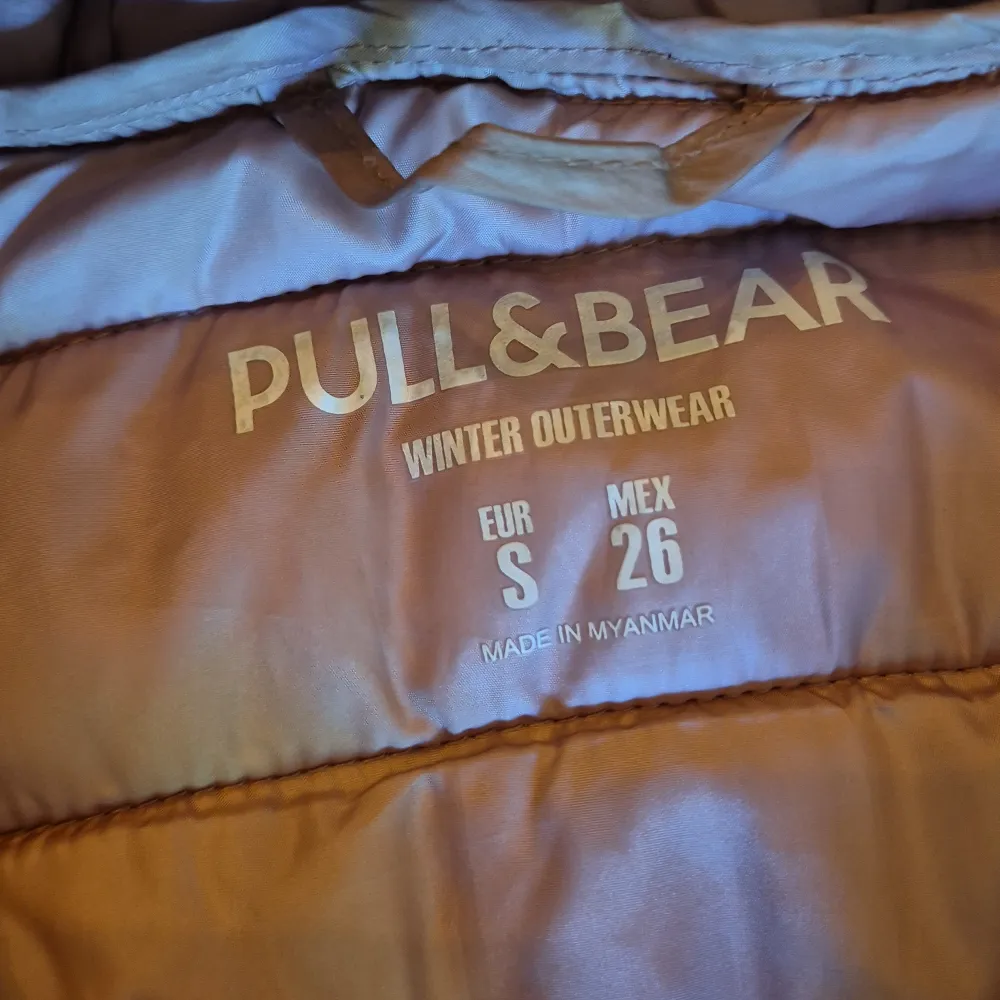 Säljer en snygg beige dunväst från Pull&Bear i storlek S. Västen har en dragkedja framtill och två fickor med dragkedjor. Den är perfekt för vintern och håller dig varm och bekväm. Västen har en huva som ger extra skydd mot kylan. Perfekt för både vardag och utomhusaktiviteter!. Jackor.