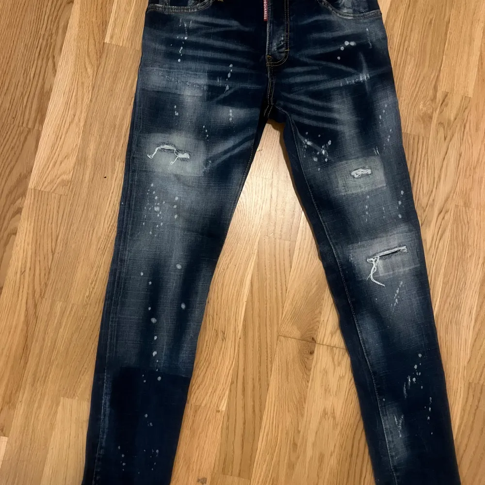 Säljer ett par snygga mörkblå jeans från Dsquared2 i storlek 42. De har en cool distressed look med slitningar och färgstänk. Perfekta för en casual och trendig stil. Jeansen har en dragkedja och knappar framtill. jeansen är äkta ! endast seriösa köpare .. Jeans & Byxor.