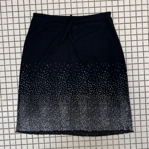 Svart kjol med vita prickar från Quelque - Säljer en superfin svart kjol från Quelque med glittriga prickar som skapar en snygg gradient-effekt. Kjolen har en knytning i midjan för en justerbar passform. Perfekt för festliga tillfällen eller en utekväll! 🖤✨