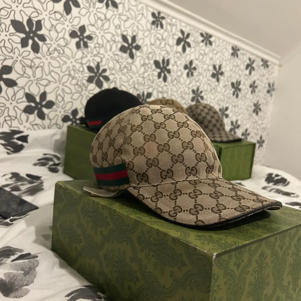Säljer en snygg beige keps från Gucci med det klassiska GG-mönstret. Kepsen har en justerbar rem baktill och en grön och röd rand på sidan. Perfekt för att ge din outfit en lyxig touch!. Asusteet.