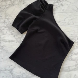 Svart oneshoulder topp - Snygg svart oneshoulder topp i ett mjukt och stretchigt material. Perfekt för en utekväll eller fest! Den har en unik design med en ärm och en axel bar. 