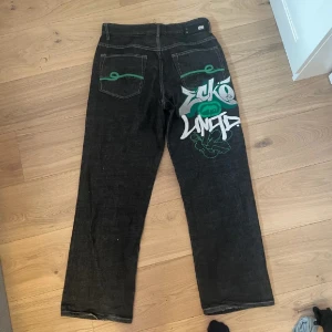 Svarta jeans med graffiti-design - Säljer ett par svarta jeans från Ecko Unltd med cool graffiti-design i grönt och vitt på baksidan. Bra skick och har baggy passform. Passar mig som är 169 cm lång💗