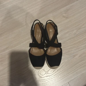 Svarta kilklackar från H&M - Snygga svarta klackar från H&M i storlek 38. De har en bekväm kilklack och är perfekta för sommarens alla tillfällen. Skorna har en stilren design med remmar som ger bra stöd. Perfekta för både vardag och fest!