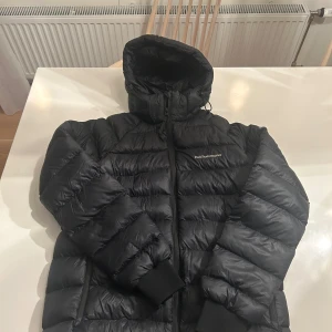 Svart dunjacka från Peak Performance - Säljer en svart dunjacka från Peak Performance i mycket bra skick. Jackan är perfekt för vintern med sin pufferstil och långa ärmar. Den har en praktisk dragkedja och en mysig huva för extra värme. Perfekt för kalla dagar! ❄️