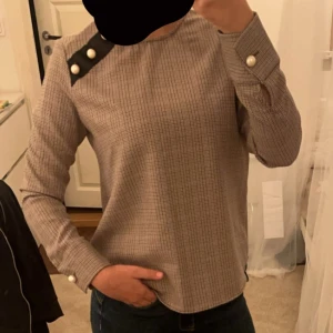 Rutig blus med pärldetaljer - Säljer en stilren rutig blus med långa ärmar och snygga pärldetaljer vid axeln och ärmsluten. Perfekt för både vardag och fest! 🖤