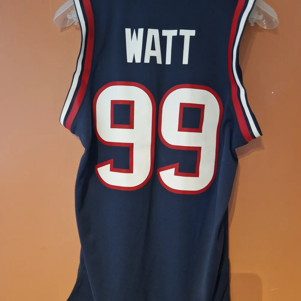 Säljer ett blått Texans linne från Nike med nummer 99 och texten 'WATT' på baksidan. Perfekt för sportiga tillfällen eller som en cool vardagstopp. Linnet är i bra skick och har en bekväm passform. Passa på att köpa denna unika sporttröja!. Tröjor & Koftor.