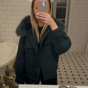 Meotine jacka - Snygg mörkgrön jacka med päls på kragen. Den har långa ärmar och knappar framtill. Perfekt för höst och vinter, med en stilren och elegant look. Jackan har två fickor med lock på bröstet. Nypris 3000kr men säljer för endast 1599!💕