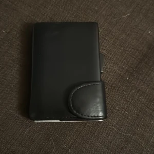 Svart plånbok i skinn. Nypris 600kr - Säljer en stilren svart plånbok i skinn. Den har en praktisk knappstängning och flera fack för kort och sedlar. Perfekt för dig som vill ha en kompakt och elegant plånbok. Passar både till vardags och fest!