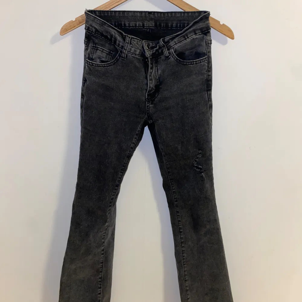 Ett par mörkgråa jeans i bra skick med en slitning på ena benet. De har en tight passform och bootcut. Jeansen är avklippta längst ner och är mellan lågmidjade och mid. Innerbenslängd: 73 cm.   Midja: 73 cm och lite stretch.. Jeans & Byxor.