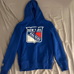 Blå New York Rangers hoodie - Säljer en snygg blå hoodie med New York Rangers-logga på bröstet. Den är officiellt licensierad av NHL och har en bekväm passform. Köpte den för några år sedan för 700kr men har bara använt några få gånger.       Storlek: S. Skriv för mer info eller annat. 💙