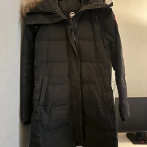Canada Goose äkta  - Säljer en svart dunjacka från Canada Goose i  bra skick. Jackan har en mysig pälsdetalj på huvan och långa ärmar. Perfekt för kalla vinterdagar med sin varma och skyddande design. Den har en dragkedja framtill och praktiska fickor. Passar perfekt för vinterns alla äventyr! ❄️