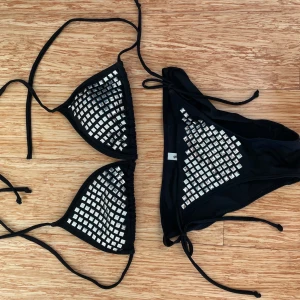 Svart bikini med silverdetaljer från Gina Tricot - Snygg svart bikini från Gina Tricot i storlek S. Den har coola silverdetaljer som ger en glittrig look. Bikinin har knytband för justerbar passform och är perfekt för sommarens stranddagar. Materialet känns bekvämt och stilrent. Perfekt för dig som vill sticka ut lite extra! ✨