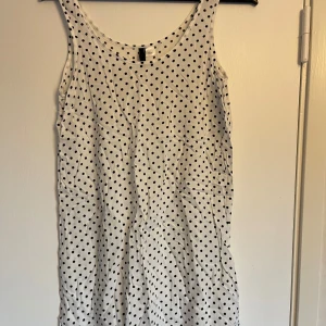 Vit prickig klänning - Säljer en söt vit klänning med svarta prickar. Den är ärmlös och perfekt för sommardagar. Klänningen har en enkel och bekväm passform, vilket gör den idealisk för både vardag och festliga tillfällen. Ett måste i garderoben för den som älskar prickigt! Kortare i längden. 