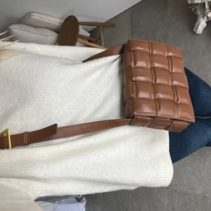 Bottega liknande väska - Säljer en superfin brun axelväska i skinn med quiltad design. Den har en justerbar axelrem med guldfärgad spänne. Perfekt för både vardag och fest! 👜✨