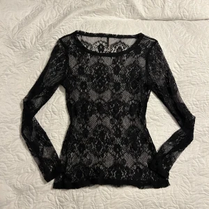 Svart spetstopp - Säljer en snygg svart spetsblus med långärmad design. Blusen är genomskinlig och har ett vackert mönster. Perfekt för en utekväll eller fest! 