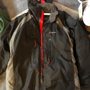 Svart och grå vindjacka från O'Neill - Säljer en svart och grå vindjacka från O'Neill i bra skick. Den har en röd dragkedja och flera praktiska fickor. Perfekt för höst och vår, med långärmade ärmar och en sportig look. Passar bra för utomhusaktiviteter och vardagsbruk.