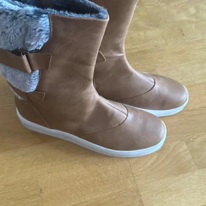 Bruna vinterstövlar med pälsdetaljer - Säljer ett par snygga bruna stövlar i syntetmaterial med mysig päls på insidan och utsidan. Perfekta för vintern med sin varma och bekväma design. De har en vit sula och är i mycket bra skick. Passar perfekt för kalla dagar! köpt från zalando