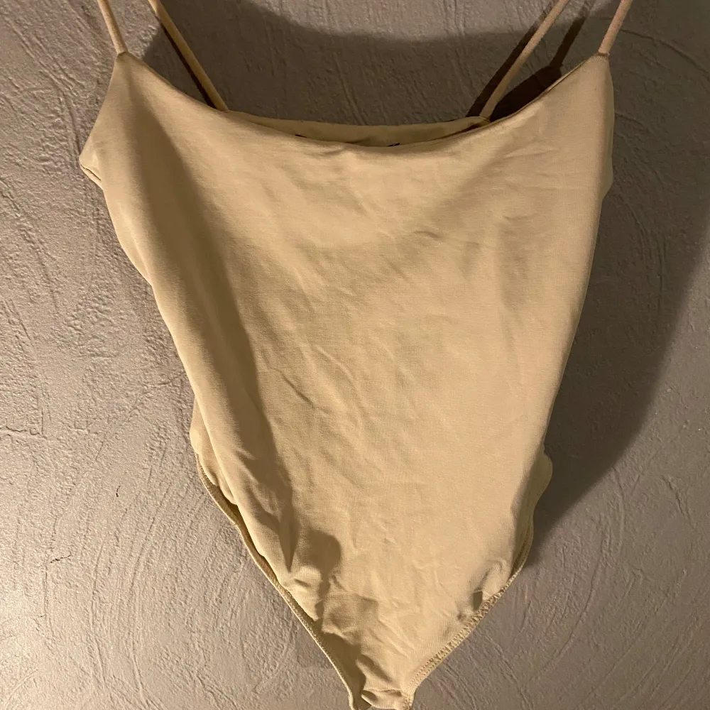 Säljer en stilren beige body med string och smala axelband. Den har en enkel och elegant design som passar alla tillfällen. Materialet känns mjukt och bekvämt mot huden. Passar perfekt för sommaren! 🌞 (PM OM DU VILL HA FLER BILDER). Toppar.