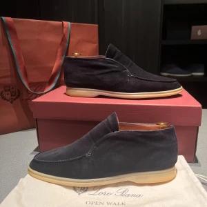 Mörkblå Open Walk från Loro Piana - Säljer ett par eleganta svarta loafers i mocka från Loro Piana. De har en stilren design med ljus sula och är perfekta för både vardag och fest. Skorna är i mycket bra skick och kommer med originalförpackning.