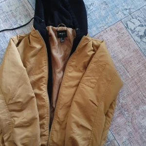 Brun jacka med huva från Forever 21 - Säljer en snygg brun jacka från Forever 21 i storlek S. Jackan har en svart huva och dragkedja framtill. Perfekt för höst och vår med sin stilrena design och praktiska fickor. Passar både till vardags och lite mer avslappnade tillfällen. 🧥🍂