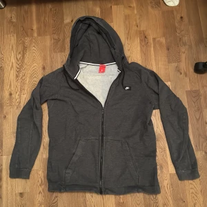 Grå zip-hoodie från Nike - Säljer en grå zip- hoodie från Nike i storlek L. Den har en dragkedja framtill och en praktisk huva. Perfekt för höst och vår, med en bekväm passform och långa ärmar. Den är i bra skick och redo för nya äventyr!