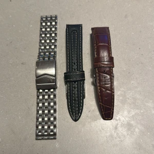 Tre klockarmband i olika material - Säljer tre klockarmband: ett i silverfärgat metall med klassisk länkdesign, ett i svart skinn med elegant söm och ett i brunt skinn med krokodilmönster. Perfekt för att byta stil på din klocka beroende på tillfälle. Alla i mycket bra skick!