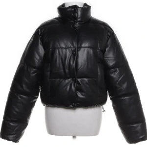 Svart pufferjacka ZARA - Snygg svart pufferjacka med hög krage och knappar framtill. Jackan har en glansig yta och är perfekt för kyligare dagar. Den har en kortare passform som ger en modern look.