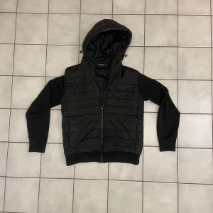 Svart jacka/cardigan från J.Lindeberg - Snygg svart jacka från J.Lindeberg. Jackan har långa ärmar och är quiltad för extra värme. Perfekt för början av våren. Priset är 1700kr kan gå ner i pris vid snabbt köp